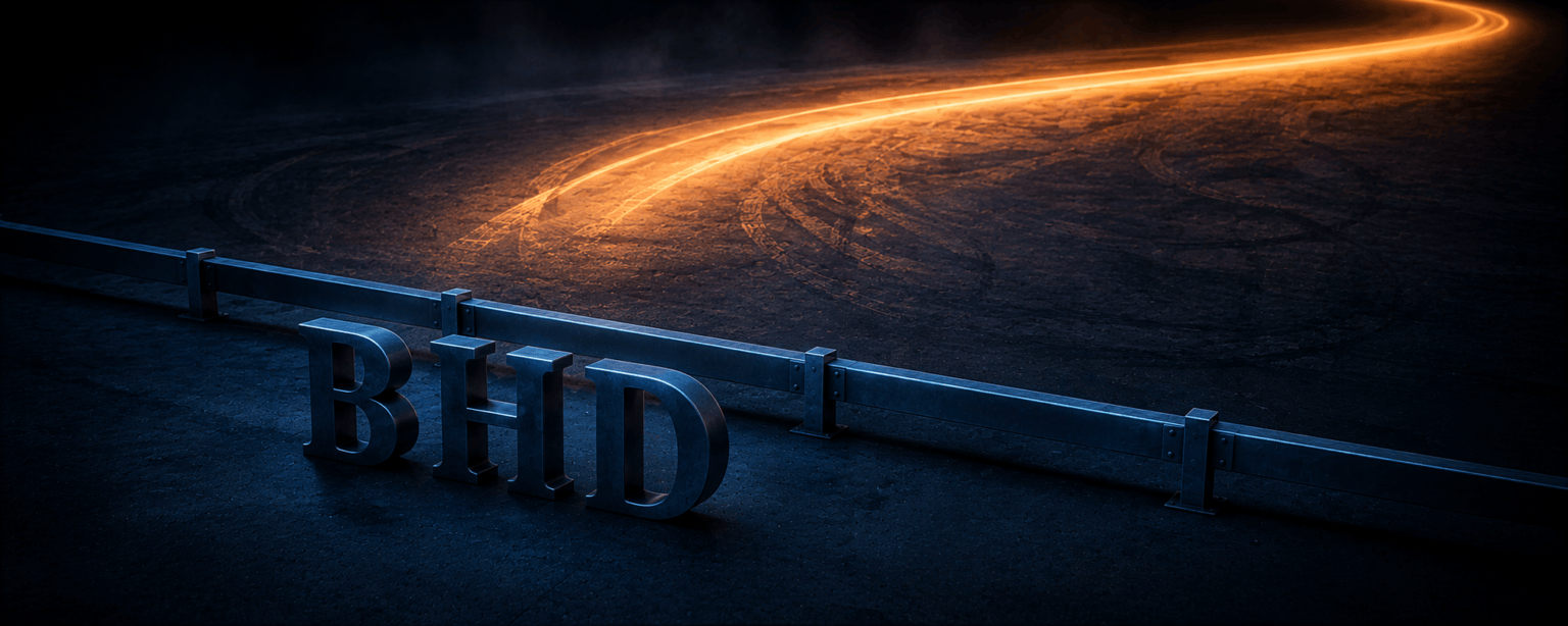 A wide amber band of light sweeping across dark asphalt and out past the frame, with the BHD letterforms fenced off in shadow behind a low steel barrier
